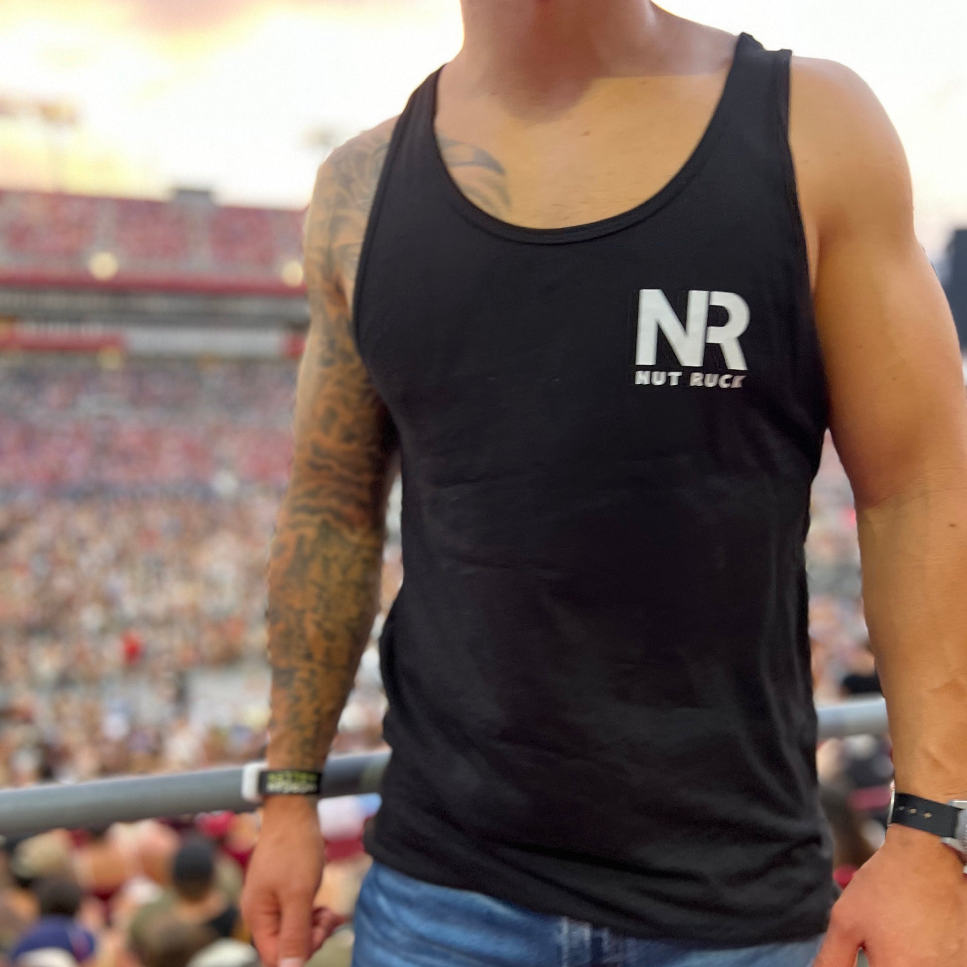 Nut Ruck Original Tank top in Black worn by a man with an athletic build and tattoos with a stadium of people behind him.