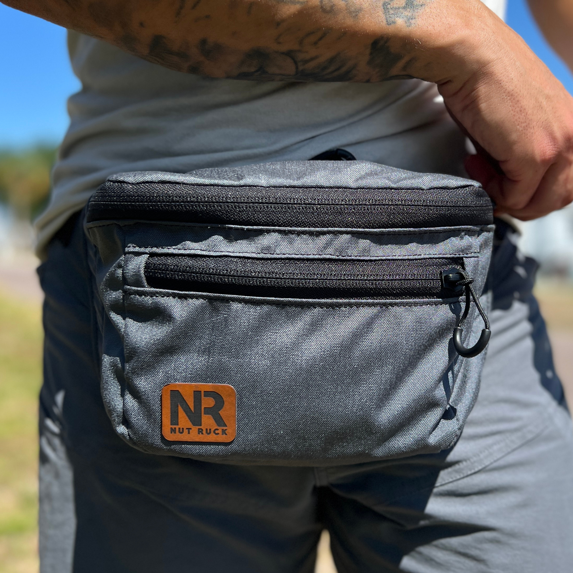 The OG Nut Ruck waist pack in Wolf Grey worn by a man in grey shorts with tattoos