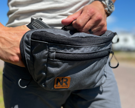 The OG Nut Ruck waist pack in Wolf Grey worn by a man who is drawing a concealed firearm from the dedicated pocket