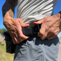 The OG Nut Ruck waist pack in Wolf Grey worn by a man who is wearing grey shorts who is buckling the pack