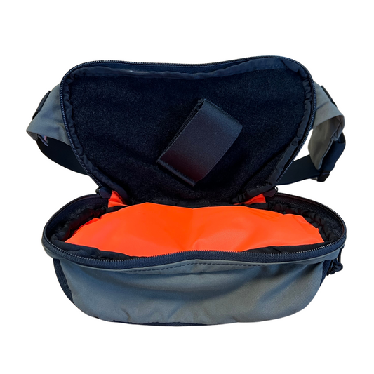 A Ranger Green OG Nut Ruck waist pack with the CCW pocket open showing the fluorescent orange interior with the black loop velcro and elastic holster attached.